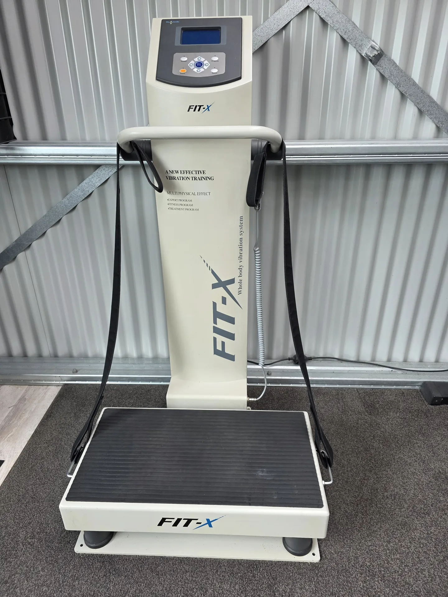 Cream Fit-x upright vibration machine with a control panel and straps